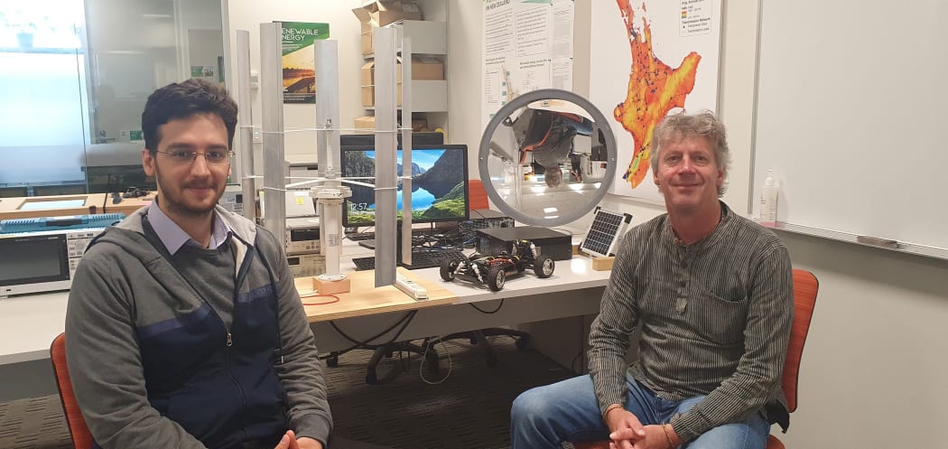 Soheil Mohseni and Alan Brent work with sustainable energy systems. There are mini versions of a vertical wind turbine and a solar concentrator on the desk behind them.