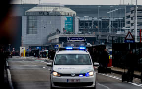 A Belgian police vehicle driving past passengers who are evacuating the Brussels Airport of Zaventem.
