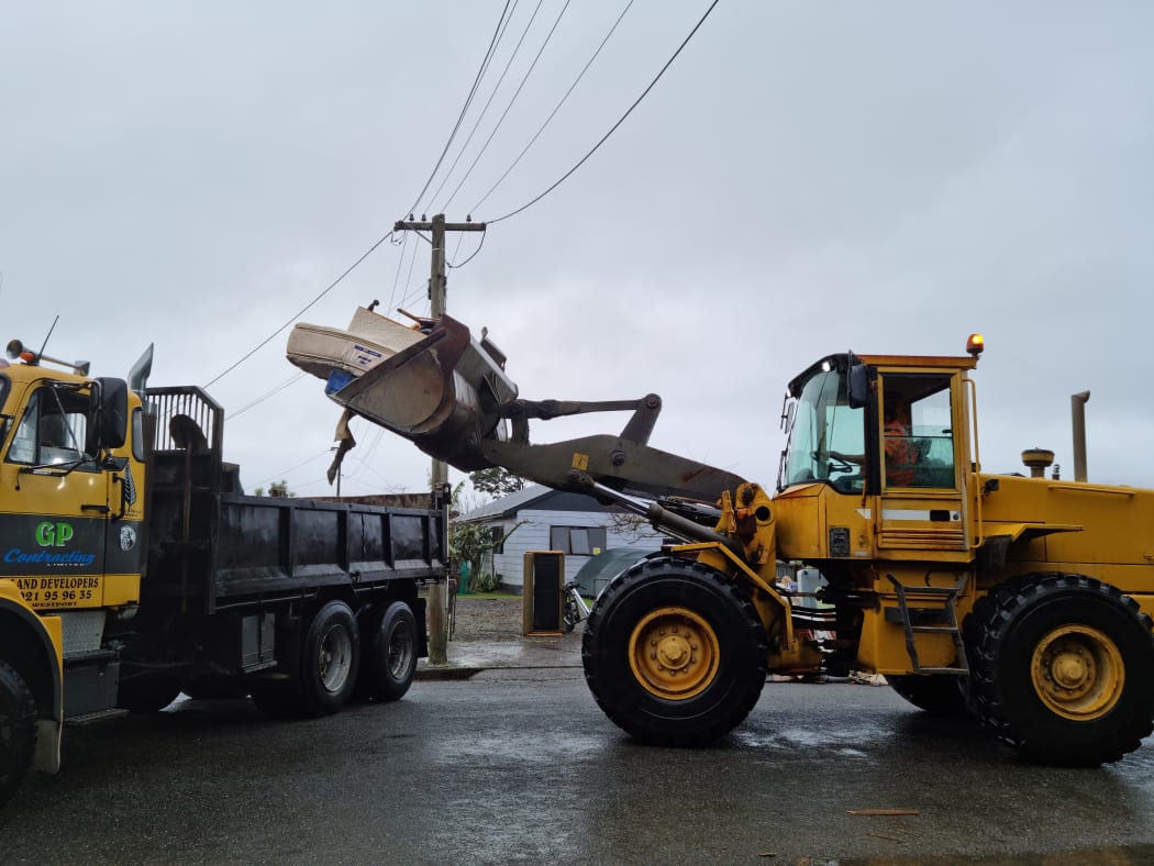 Couches and furniture are being carried out of homes and loaded with diggers into trucks to be taken away and disposed of.