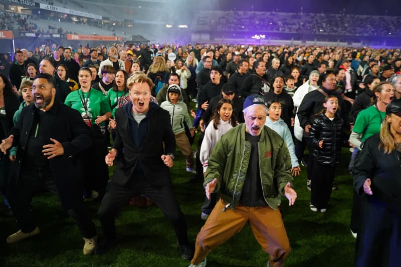 American TV host and comedian Conan O'Brien (centre) does the haka with Kiwi director Taika Waititi (right) and thousands of people at Eden Park for the world record on 29 September, 2025.