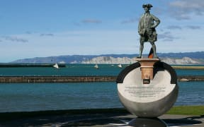 Cook and Vaka - a flotilla of sailing va'a cruise offshore of a statue of James Cook on the Gisborne foreshore