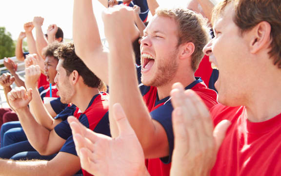 A photo of a line of spectators in red clothing, shouting and clapping in support of their team.