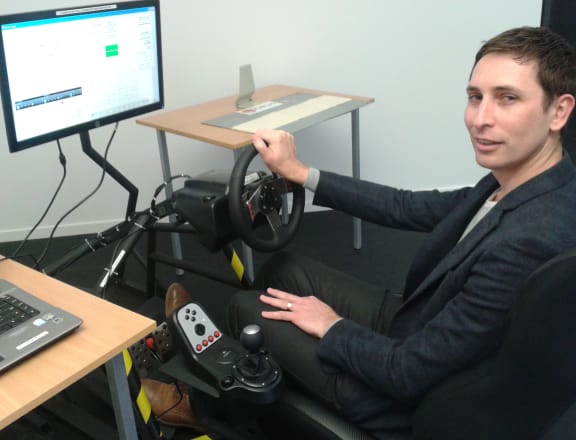 Behavioural scientist Jared Thomas seated at OPUS Research's audio tactile profile simulator, which is used to test how people detect rumble strips of different heights and spacings.