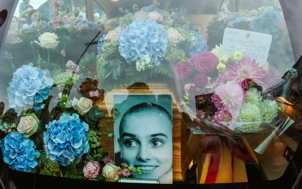 A photograph taken on August 8, 2023 shows the coffin and a picture of late Irish singer Sinead O'Connor, in the hearse during her funeral procession outside her former home in Bray, eastern Ireland, ahead of her funeral on August 8, 2023. A funeral service for Sinead O'Connor, the outspoken singer who rose to international fame in the 1990s, is to be held on Tuesday in the Irish seaside town of Bray. (Photo by PAUL FAITH / AFP)