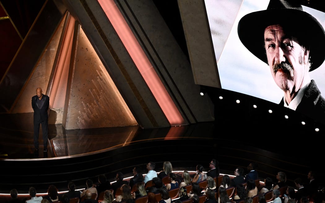 An image of late US actor Gene Hackman is seen on a screen as US actor Morgan Freeman stands onstage during the 97th Annual Academy Awards at the Dolby Theatre in Hollywood, California on March 2, 2025. (Photo by Patrick T. Fallon / AFP)