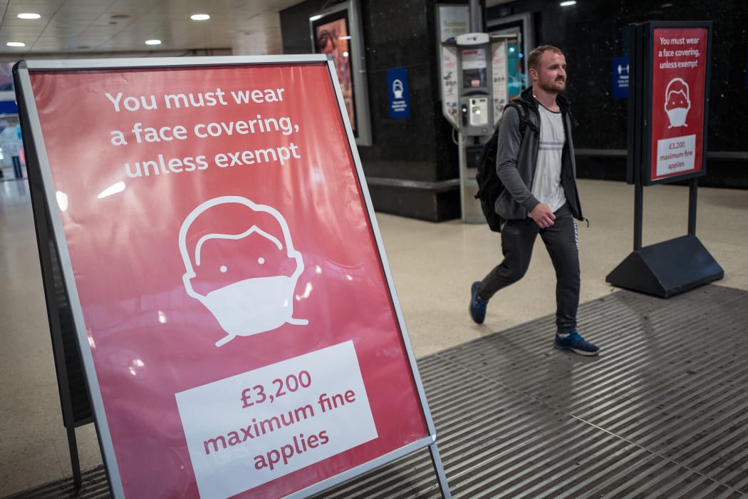 A man, not wearing a face covering, passes signs telling travellers they must wear face mask unless they are exempt, as he leaves Victoria station during the evening 'rush hour' in central London on September 23, 2020. -