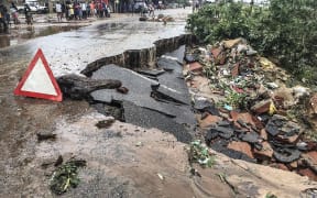 Residents stand next to a road partially destroyed by Cyclone Kenneth.