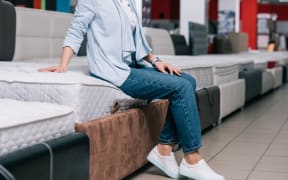 Shopper sits on mattress at furniture shop.