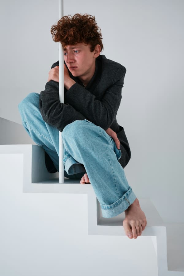 A sad-looking redheaded boy leans against a white pool and looks near tears.