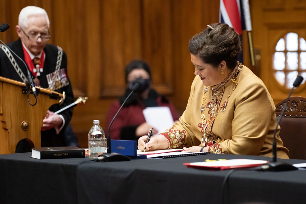 Dame Cindy Kiro signs the oaths while Herald of Arms Phillip O'Shea hovers, watching it's done right and waiting for his proclamation
