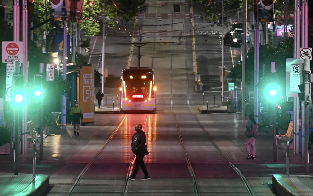 A man crosses a street moments before a night-time curfew is lifted in Melbourne on October 21, 2021, as one of the world's most locked-down cities reopened, with Melbourne residents hoping this sixth bout of stay-at-home restrictions will be their last. (Photo by William WEST / AFP)