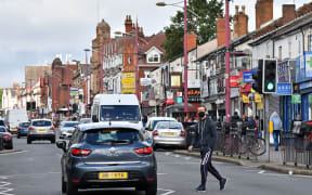 A man wearing a protective face mask crosses Soho Road in the Handsworth area of Birmingham, central England on August 22, 2020.