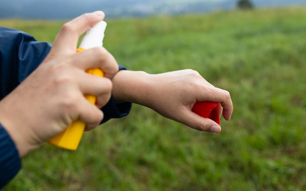 Young backpacking tourist using anti mosquito, insect repellent spray outdoors at hiking trip.