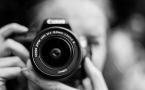 A person holding a camera to their fdace, in black and white.