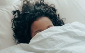 woman hiding under bedsheet