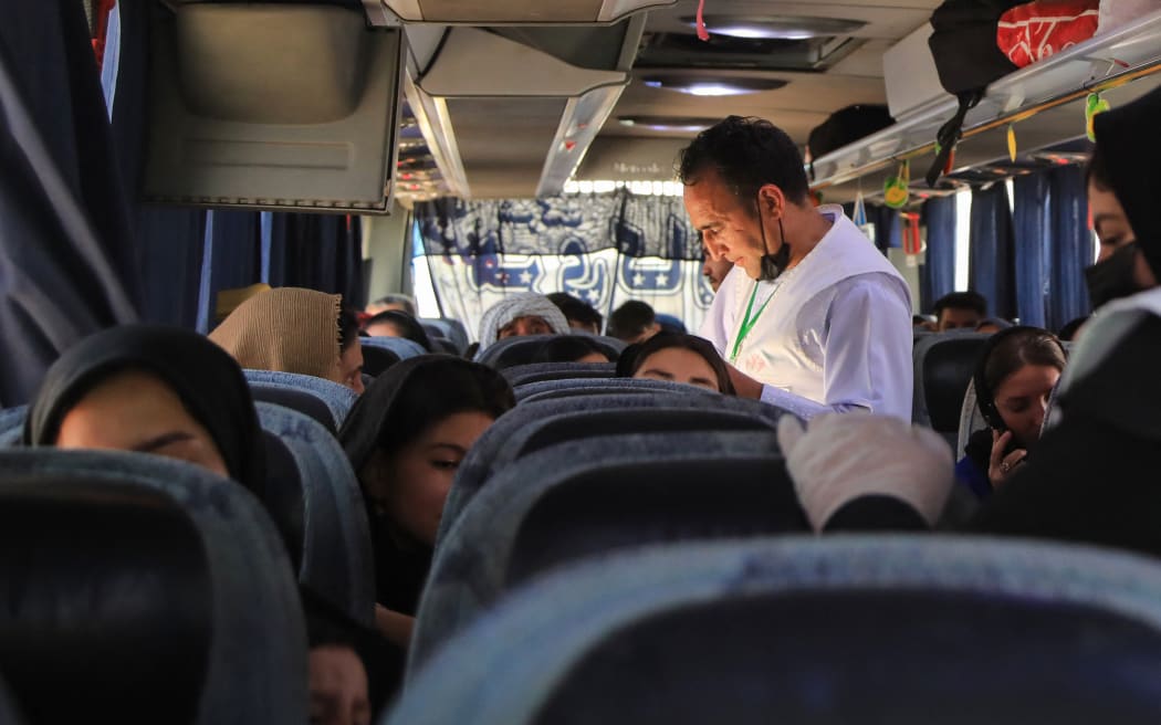 This photograph taken on July 24, 2025 shows Abdul Qadir Salehi (C), an Afghan volunteer checking a name list of the newly arrived Afghan migrants deported from Iran, inside a bus at the Islam Qala border crossing in Herat province. At the border with Iran, volunteers distribute food and hygiene products to Afghans forced back to their country, unable to watch on as a migrant crisis grows. Since the beginning of 2025, more than 1.6 million Afghans, including many children, have crossed the border after being deported or driven out of Iran, which accuses them of feeding unemployment and crime. (Photo by Mohsen KARIMI / AFP) / TO GO WITH 'AFGHANISTAN-IRAN-MIGRATION' REPORTAGE