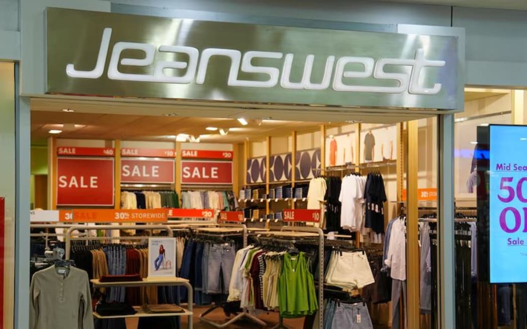 A storefront with red sale signs inside and a big white sign reading 'Jeanswest'.