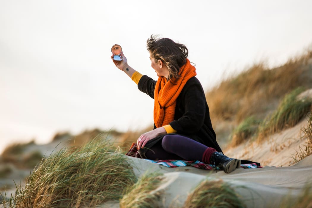Woman looking at compact mirror on beach (Photo by Tom Dunkley / Connect Images / Connect Images via AFP)