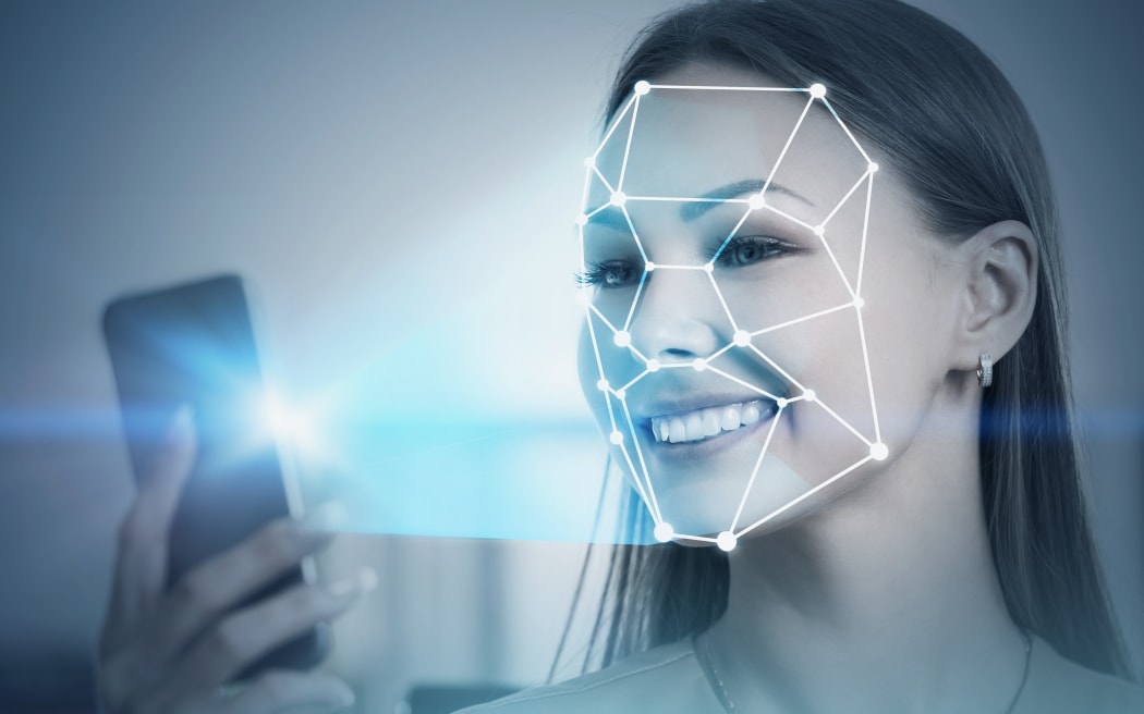 Smiling blonde businesswoman in dress using smartphone with face recognition technology in blurred office. Toned image double exposure