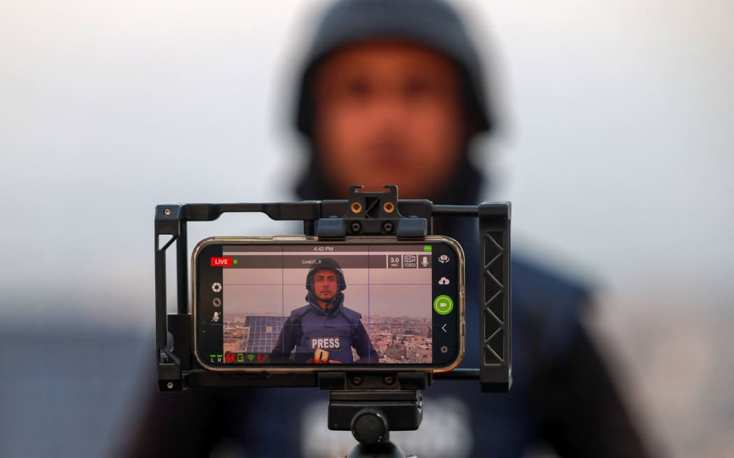 A Palestinian journalist uses the mobile phone to broadcast live in Rafah on the southern Gaza Strip on December 27, 2023, amid continuing battles between Israel and the Palestinian militant group Hamas. Power cuts have become a fact of life in war-torn Gaza. But thanks to embedded SIM cards, Palestinians can still access the internet and stay in touch with loved ones abroad. (Photo by SAID KHATIB / AFP)