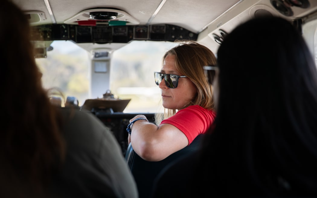 Lydia Green is wearing a red tshirt and sunglasses and rests her arm on the back of a seat while sitting onboard a small plane.