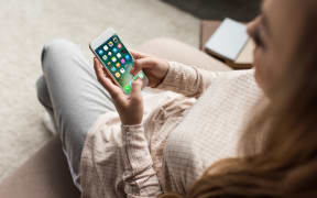 cropped shot of woman on couch using smartphone with ios apps on screen