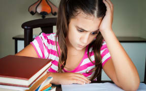 14796085 - angry and tired schoolgirl studying with a pile of books on her desk