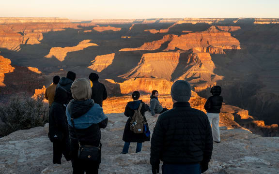 GRAND CANYON, ARIZONA - FEBRUARY 22: Tourists overlook the Grand Canyon at sunrise on February 22, 2025 in Grand Canyon, Arizona. The Trump administration is planning to restore jobs for dozens of National Park Service employees after laying off approximately 1,000 probationary employees amid a wave of federal work force cuts. In addition, the Trump administration has pledged to restore 50 jobs along with the hiring of an additional 3,000 seasonal workers.   Brandon Bell/Getty Images/AFP (Photo by Brandon Bell / GETTY IMAGES NORTH AMERICA / Getty Images via AFP)