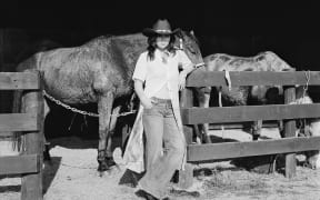 Crystal Chen - a woman wearing flared jeans and a cowboy hat - stands in front of a horse.
