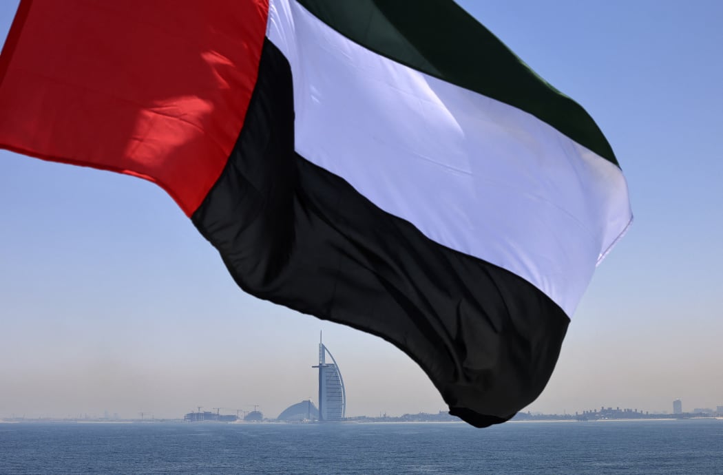 Emirati flag fluttering above Dubai's marina with the Burj Al Arab landmark hotel (C) in the background.
