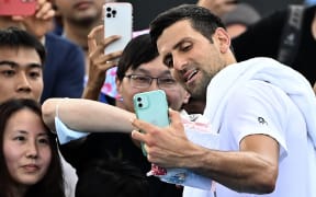 Serbia's Novak Djokovic takes selfies with fans after a practice session on day two of the Australian Open tennis tournament in Melbourne on January 17, 2023. (Photo by MANAN VATSYAYANA / AFP) / -- IMAGE RESTRICTED TO EDITORIAL USE - STRICTLY NO COMMERCIAL USE --