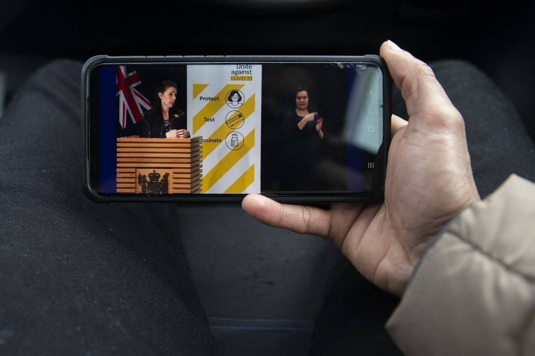 A man watches a live press conference of New Zealand Prime Minister Jacinda Ardern (L) in Christchurch, New Zealand, on August 27, 2021. Ardern has confirmed Auckland will remain in alert Level 4 lockdown until 31st August 2021 as the country battles with the latest COVID-19 outbreak.