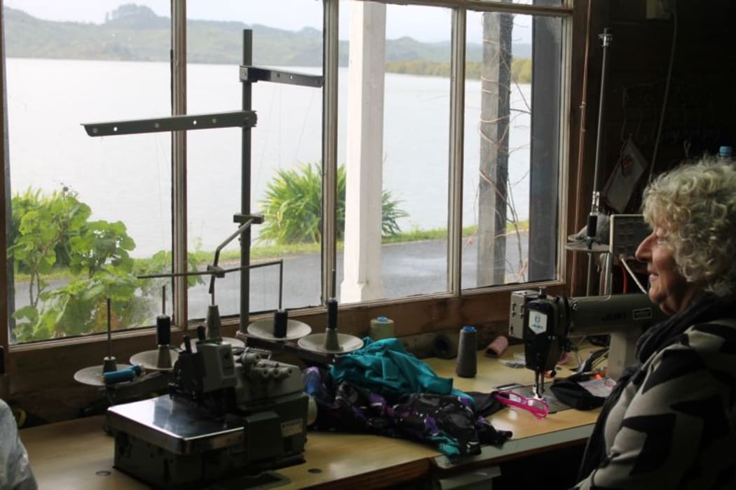 Carol sits at her sewing  machine  in the window looking on to the harbour