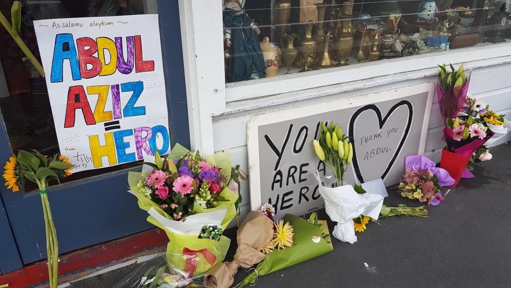 Floral tributes and signs are building up outside the shop of Abdul Aziz, who threw an eftpos machine at the attacker.