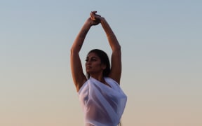 The album cover for 'Sweet Surrender'. Singer/songwriter Aaradhna poses against the background of the setting sun at the beach. Her arms in the air.