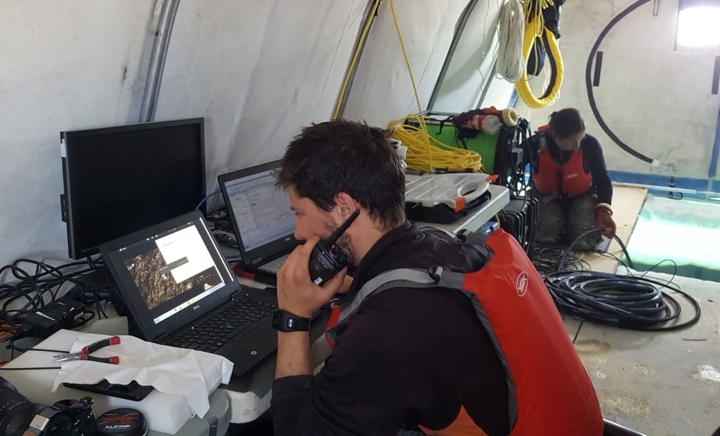 Emiliano Cimoli watches data coming in from a hyperspectral camera deployed under the sea ice. Vanessa Lucieer, at the back of the tent, feeds out cable through a hole cut in the ice.