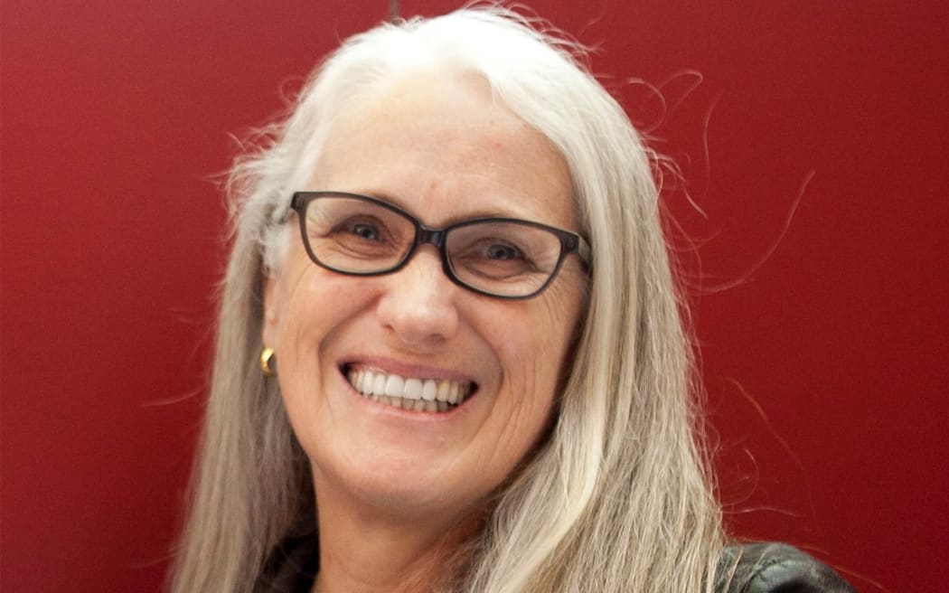 New Zealand filmmaker Jane Campion, a white woman in black glasses, smiling against a red background