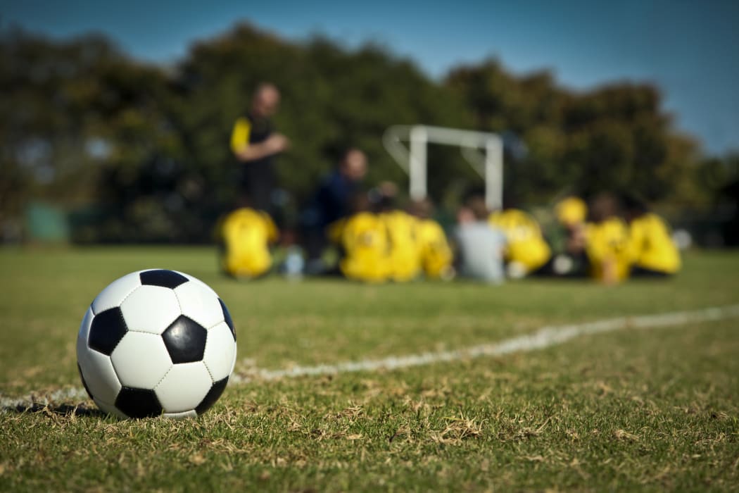 A soccer ball in the foreground, with a team of student players in the background.
