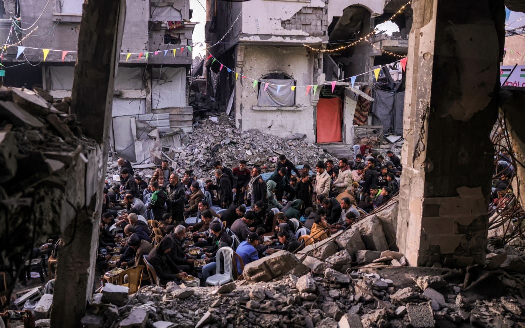 People gather for the iftar, or fast-breaking meal, on the first day of the Muslim holy fasting month of Ramadan in Jabalia in the northern Gaza Strip on March 1, 2025 by the rubble of collapsed buildings that were destroyed during the war between Israel and Hamas, amid the ongoing truce. (Photo by Bashar TALEB / AFP)