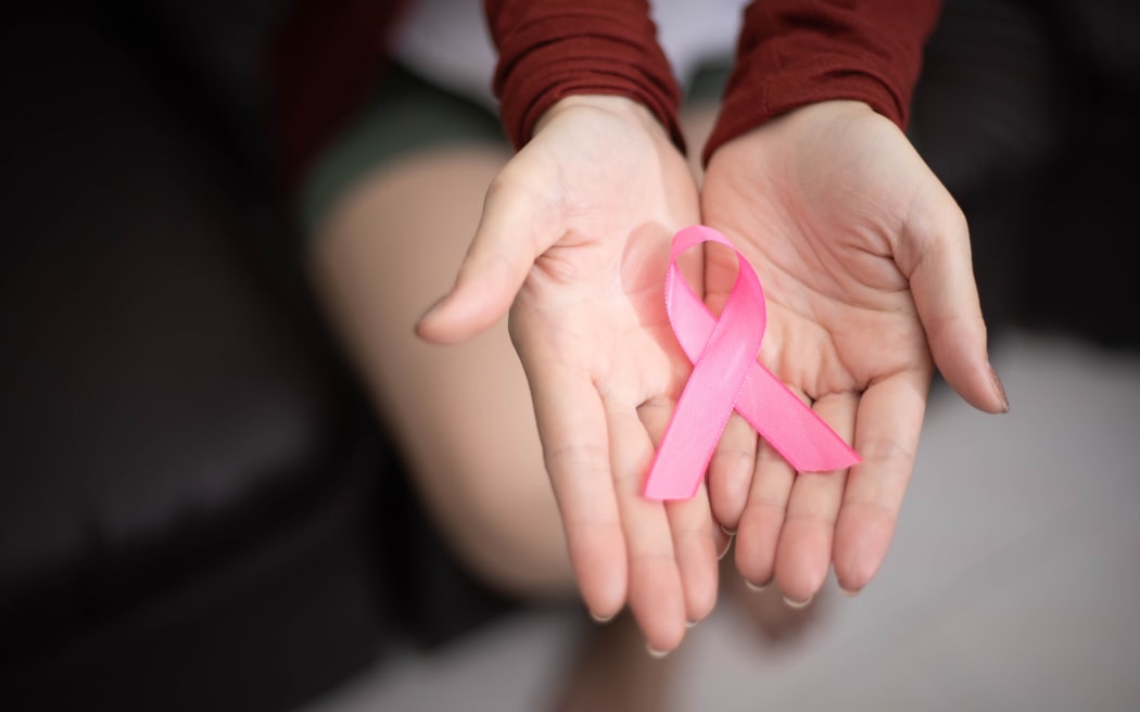 Woman holding a pink ribbon representing breast cancer awareness.