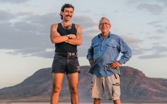 Man in his 20s wearing a singlet and short shorts with his grandad in the Australian outback.