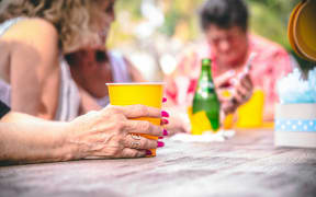 A person holds a yellow cup while sitting at a table with other people.