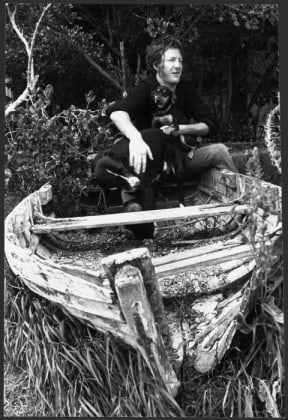 Sam Hunt with a dog and a puppy, sitting on the wreck of a row boat, at an unidentified location. Photograph taken circa 3 December 1975 by an unidentified staff photographer for the Evening Post.