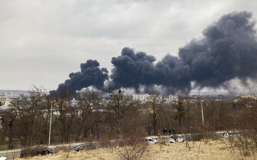 A picture taken on March 26, 2022 shows a religious statue as dark smoke rises from a fire following an air strike in the western Ukrainian city of Lviv.