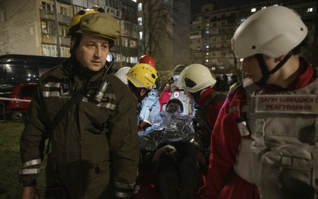 Rescuers and paramedics evacuate an elderly woman near a damaged residential building following a drone attack in Kyiv on 23 March 2025, amid the Russian invasion of Ukraine.