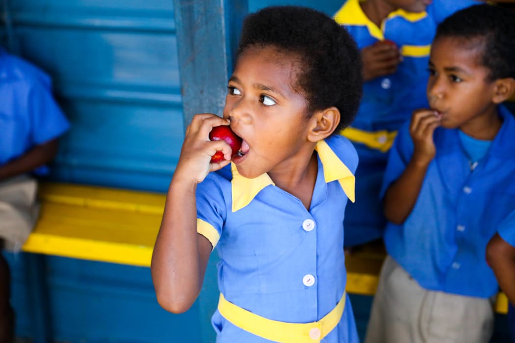 A kindergartener at Koroipita in Fiji munches on an apple. An expensive import, the fruit was a gift from the visiting New Zealand delegation