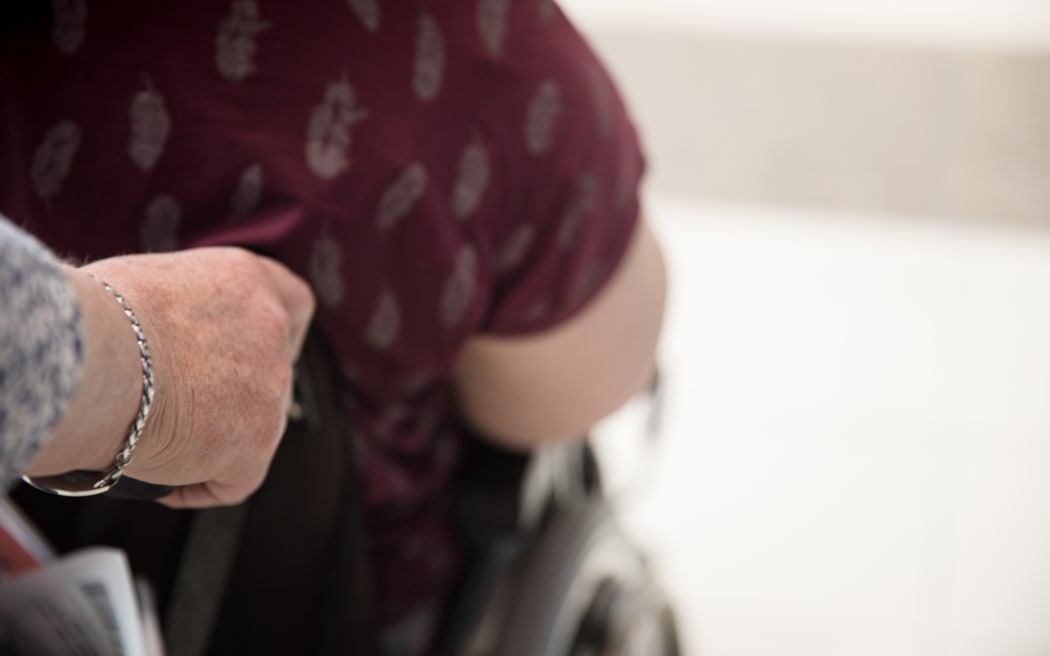 A mother pushes her adult daughter around a shopping mall in a wheelchair.