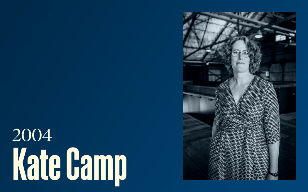 A woman in a checked dress with glasses stands in a large open room, text reads "2004, Kate Camp"