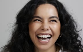 Courtney Dawson laughs. She is wearing a white shirt and a gold chain necklace.