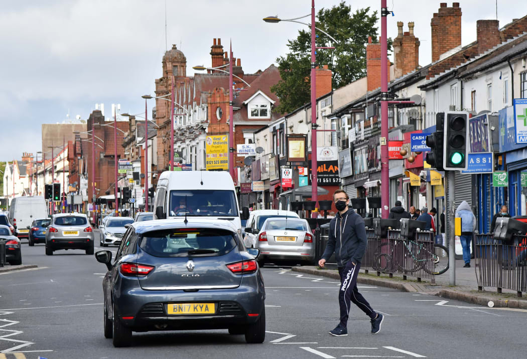 A man wearing a protective face mask crosses Soho Road in the Handsworth area of Birmingham, central England on August 22, 2020.